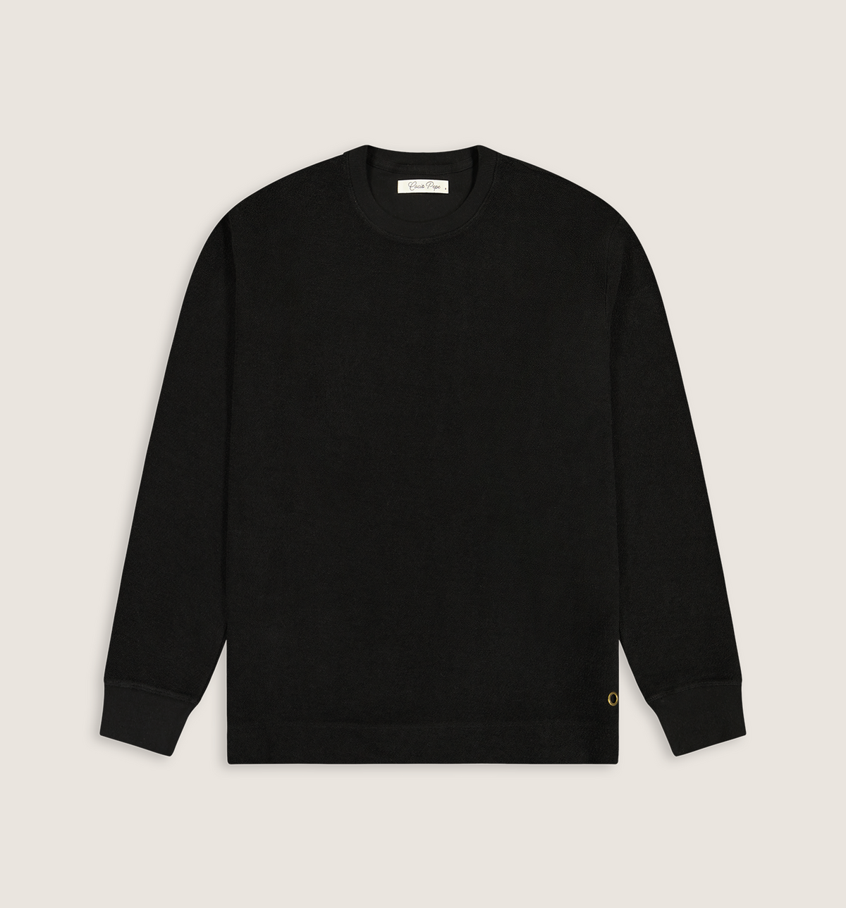 A black long-sleeve crewneck sweater laid flat against a light beige background. A small gold embroidered 'C' logo is visible on the lower left hem, and a white brand label is printed inside the collar.